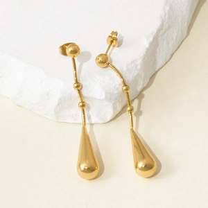 Detailed view of long gold-plated teardrop earrings displayed on a white textured stone