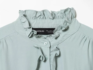 Close-up of ruffled collar and button detail on light blue viscose blouse for women