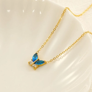 Elegant 18k gold butterfly necklace with blue and white zircons on a white shell tray