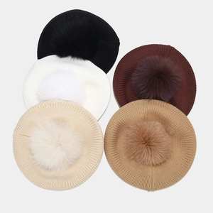Flat lay of knit beret hats in five colors featuring large fluffy fox fur pom-poms