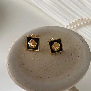 Detailed close-up of square gold seashell earrings on a ceramic tray with pearls