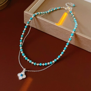 Close-up of double-layer necklace with turquoise beads and a clover-shaped floral pendant