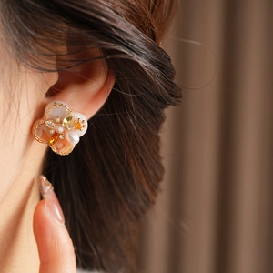 Detail of floral earring with pearls and gemstones worn on ear in warm vintage lighting