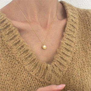 Elegant gold shell pearl necklace worn by a model in a warm brown knit sweater