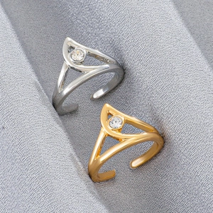 Detail view of gold and silver teardrop rings with clear gemstones on gray fabric