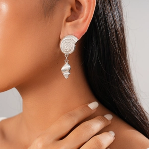 Silver shell and conch drop earrings featuring intricate pleated textures on a female model
