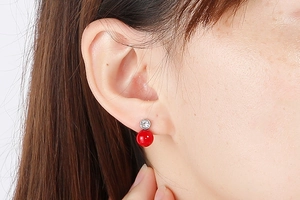 Close-up of a titanium steel stud earring featuring a red pearl and sparkling rhinestone