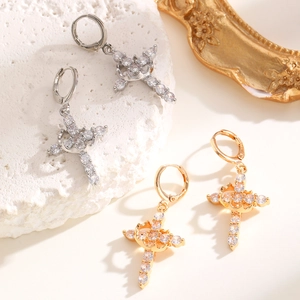 Close-up of gold and silver cross earrings with sparkling cubic zirconia on a stone surface