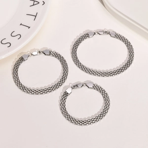 Detailed view of three-layered silver braided mesh chain bracelets on a ceramic plate