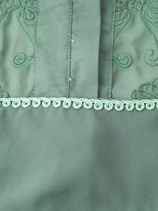 Détail d'une robe de vacances verte avec broderies et dentelle festonnée délicate