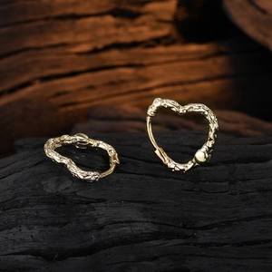 Elegant gold heart earrings with textured surface displayed on a dark wood background