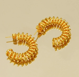 Detailed close-up of 18K gold-plated spring spiral hoop earrings on a reflective surface