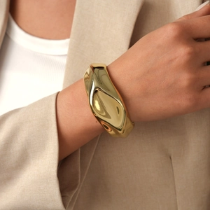 Close-up of a wide gold cuff bracelet featuring an irregular curved mirror finish on a model