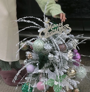 Close-up of a mini Christmas tree with white snow coating, ornaments, and a festive sign