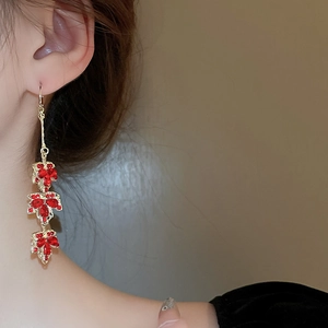 Détail de boucles d'oreilles dorées avec trois feuilles d'érable rouges serties de strass