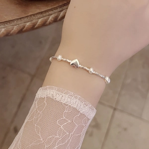 Close-up of a silver heart charm bracelet with pearls on a wrist with lace sleeve