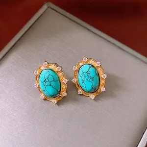 Vintage oval turquoise stud earrings with gold trim and crystal halo on gray display