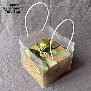 Square transparent PVC gift bag with handles holding a woven box and green silk ribbon
