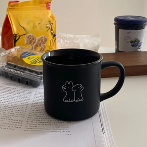 Detail of matte black ceramic mug with cartoon puppy illustration and drink more water text