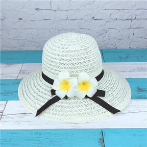 Detail view of cream straw sun hat with elegant frangipani flowers and black ribbon bow