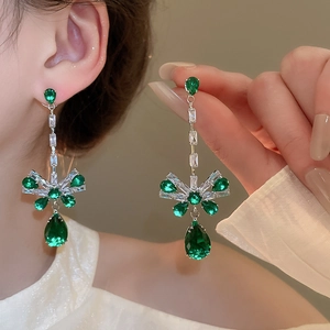 Detailed view of silver bow-shaped earrings with green and white zircons on model