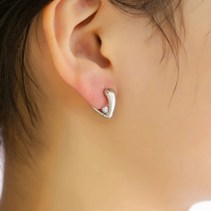 Gros plan d'une boucle d'oreille haricot en métal poli argenté sur une femme