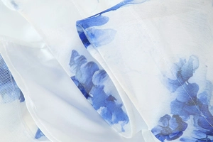 Vue macro du tissu en organza blanc avec imprimé fleuri bleu et coutures de bordure