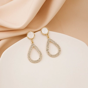 Detail of gold-plated teardrop earrings with white zircons and shell-like accents