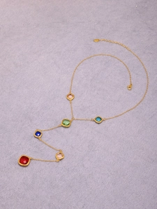 Dettaglio di una collana a Y dorata con sei vivaci pietre preziose colorate a taglio quadrato