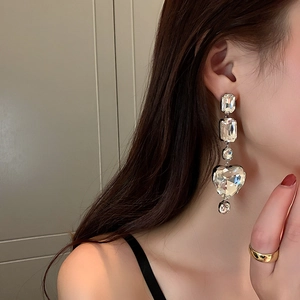 Close-up of dangling heart earrings with clear faceted crystals worn by a model