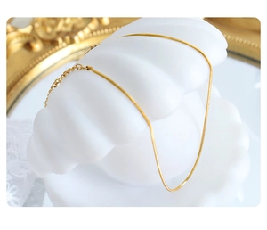 Detail of minimalist 18K gold snake chain anklet displayed on a white shell prop