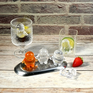 Three penguin-shaped ice cubes in orange and clear colors on a silver serving tray