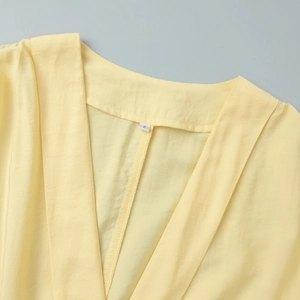 Detail shot of a soft yellow V-neckline and fabric texture on a long sleeve summer dress