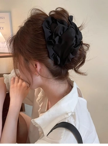 Detail of a large black fabric flower hair claw clip on a model in a warm indoor setting