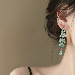 Detail of emerald green leaf drop earrings worn by a model in warm light setting