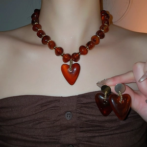 Detail of amber acrylic heart pendant necklace and matching earrings on a model