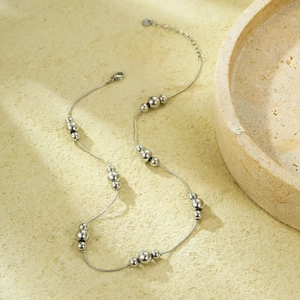 Minimalist silver snake chain necklace with polished beads on a textured stone background