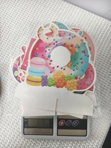 Detailansicht der Donut-Party-Bannerkarten in Kunststoffverpackung auf einer Waage