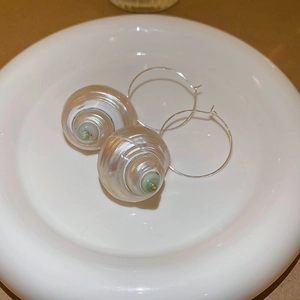 Macro detail of silver hoop earrings with pearlescent seashell charms on white ceramic tray