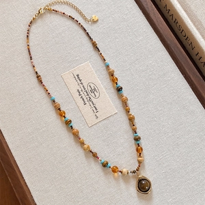 Collier de perles rétro avec pierres colorées et pendentif doré sur fond en lin