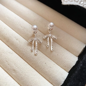 Detailed view of silver bow earrings with round pearls on a soft beige velvet background