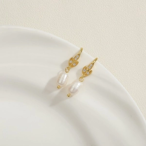 Close-up of golden leaf earrings with zircon pavé and dangling baroque pearls