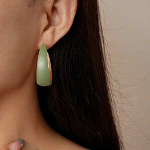 Close-up of matte green and gold hoop earrings with a modern curved design on ear