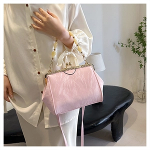 Pink pleated shell bag with pearl handle and gold clasp worn by model in white shirt