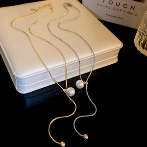 Detail view of gold and silver snake chain necklaces with pearls on a white display box