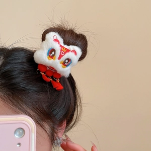 Détail de la pince à cheveux lion en peluche avec pompons rouges sur une coiffure