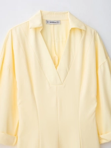 Dettaglio del colletto dell'abito giallo a maniche lunghe con scollo a V e etichetta taglia