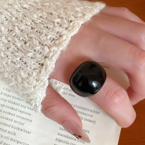 Close-up of minimalist black resin pebble ring worn with a cozy beige knit sweater