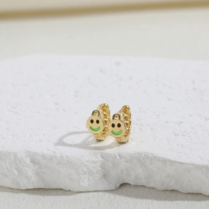Macro shot of gold hoop earrings with green enamel smiley face charms on a white stone base
