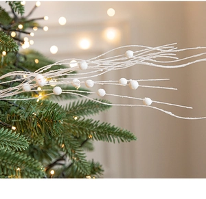 Close-up of white glittery berry picks on a green Christmas tree with warm bokeh lighting
